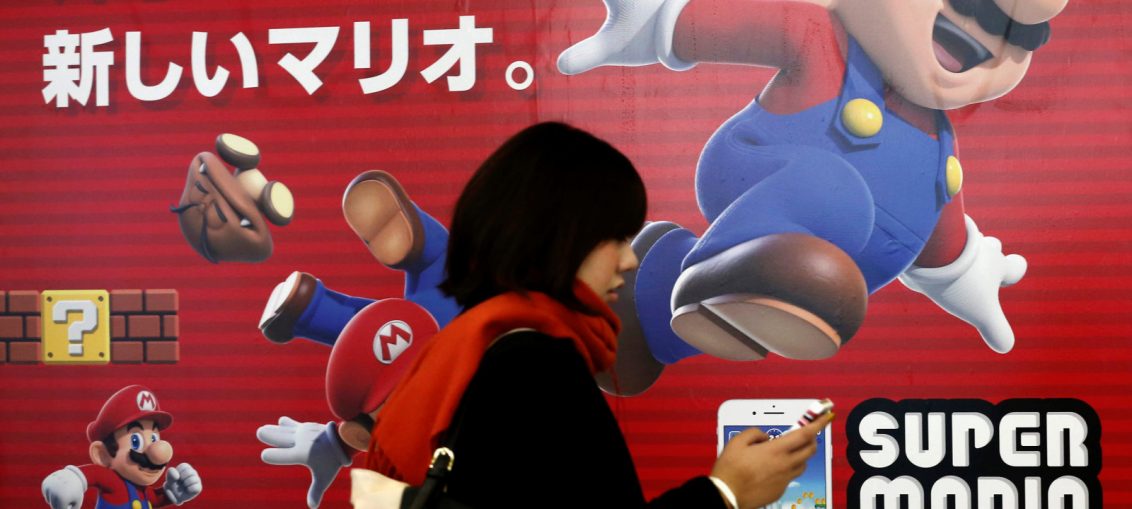 A woman using a smartphone walks past Nintendo’s “Super Mario Run” game advertisement board at a subway station in Tokyo, Japan 